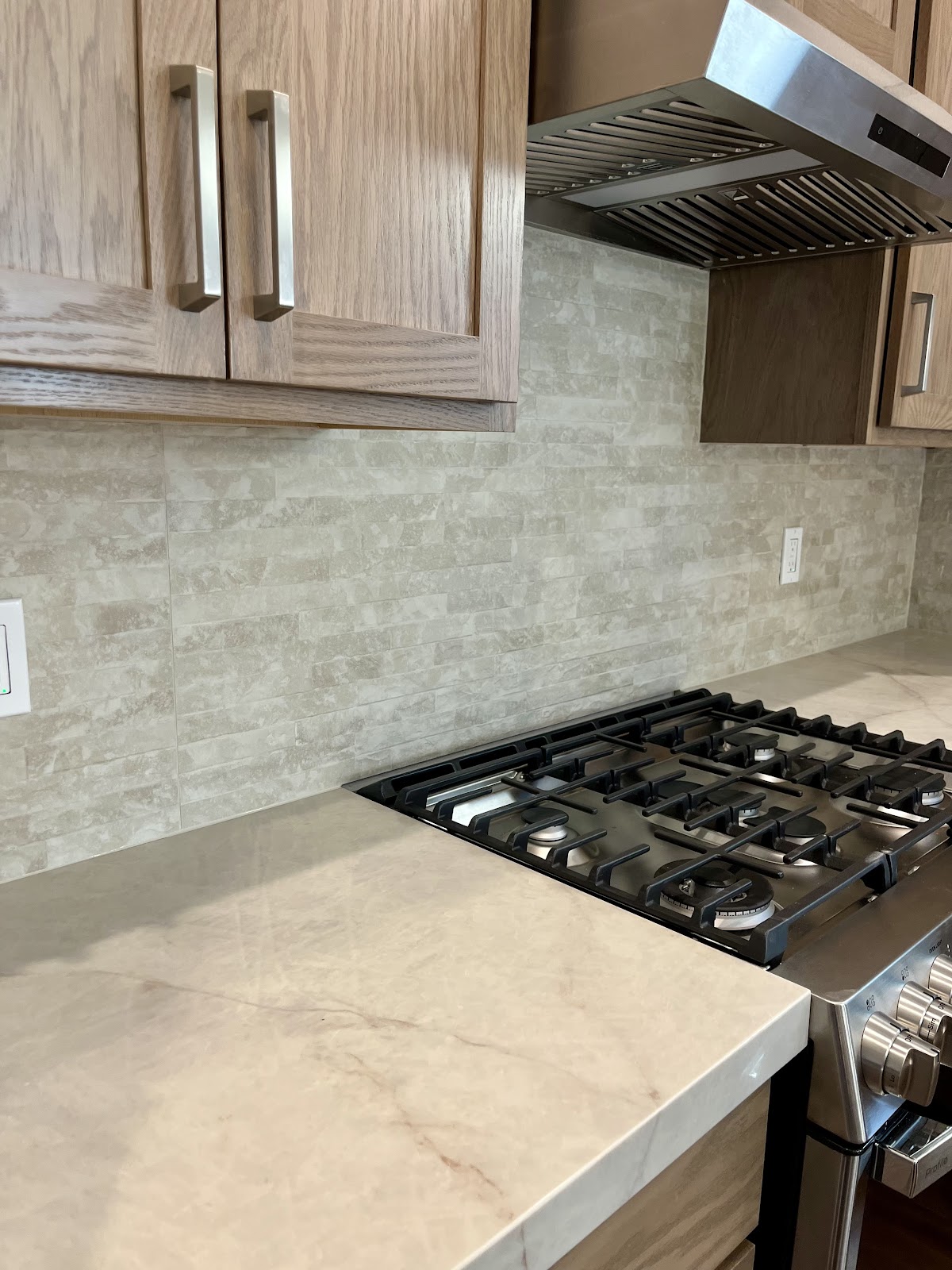 Stone tile backsplash behind a gas range with quartz counter
