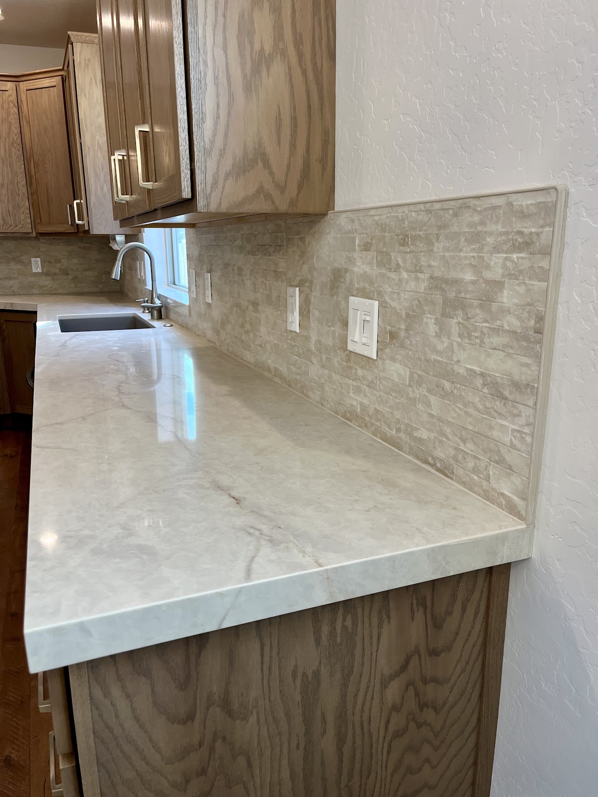 Kitchen peninsula with linear stone backsplash and marble-look counter